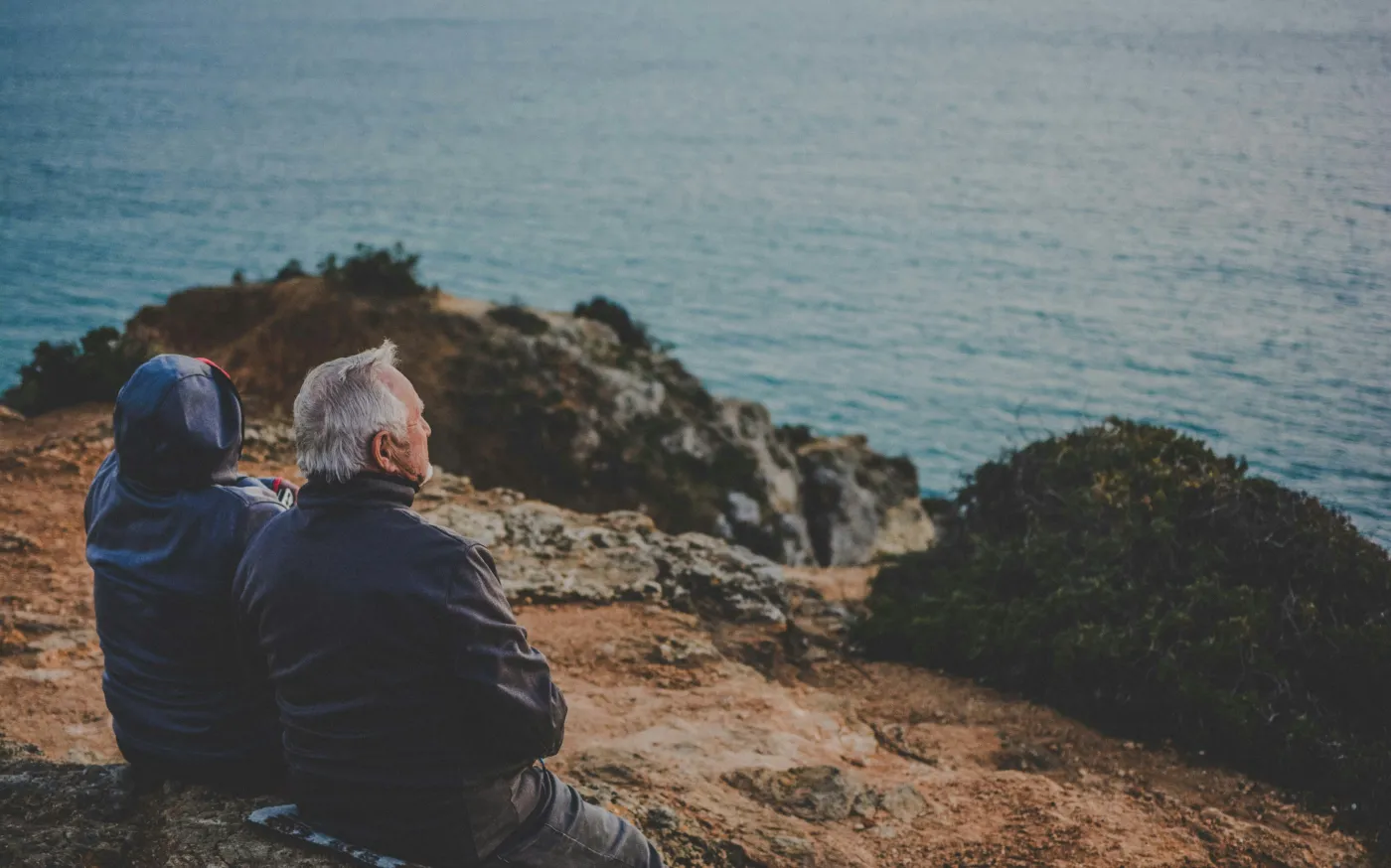 two person sitting on rock staring at body of water during daytime by Katarzyna Grabowska courtesy of Unsplash.